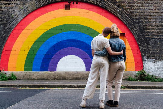 Gay couple standing together in front of rainbow colored wall