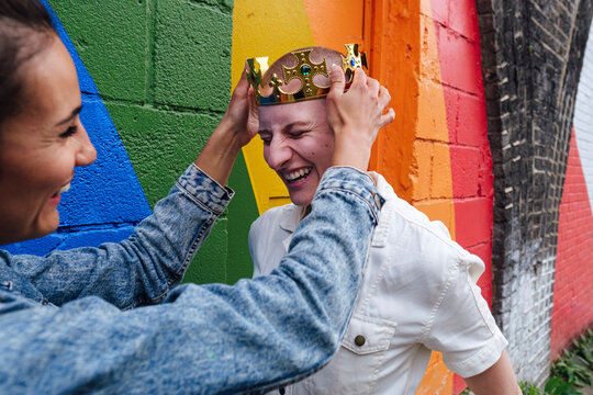 Lesbian woman keeping crown on woman's head by rainbow wall