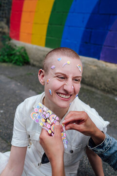 Woman sticking sticker on face of happy non-binary person
