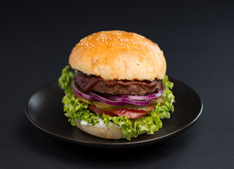 Close-up of a delicious fresh homemade burger with lettuce, cheese, onion and tomato on a rustic wooden board on a dark background