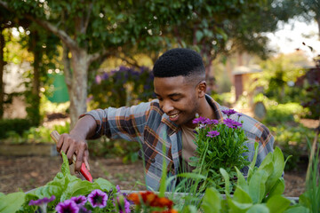 Happy young black man in checked shirt smiling while using spade in flowerbed in garden center
