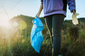 Volunteer walking in grass holding garbage bag on sunset