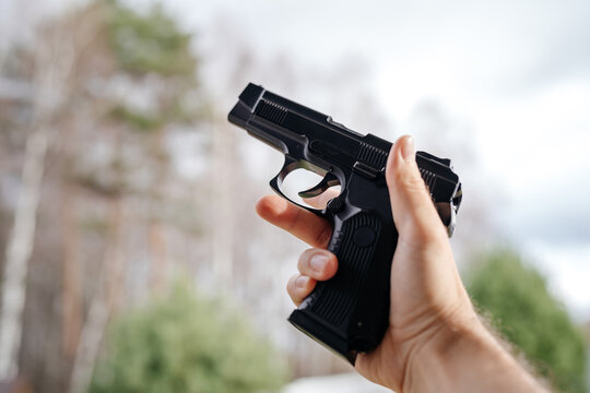 The gun in the man's hand is aimed at the background during the day. Weapons and self-defense.