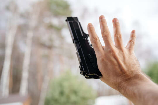 Pistol in the man's hand pointing up during the day. Weapons and self-defense or attention.