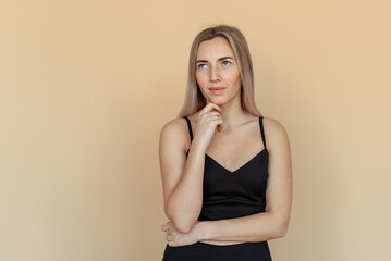 Dreamy pretty young woman with freckles touch chin thought choose decide solve problems dilemmas, wear fashionable top, stands over beige background. Thinking positive concept