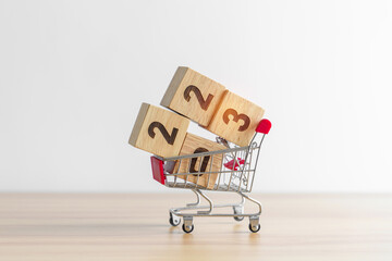 Happy new year with 2023 block in shopping trolley cart on table. E commerce, online shopping,...