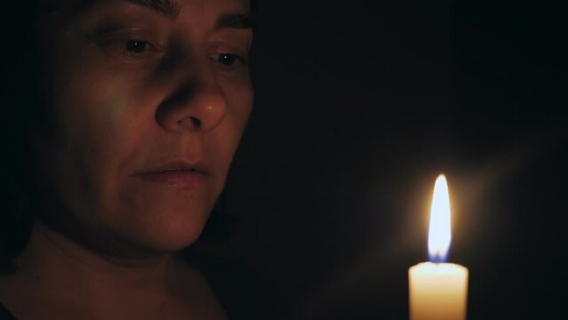 A Caucasian woman prays while standing in front of a burning candle. The girl looks at the candle, finishes her prayer, and blows out the candle.