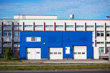Fototapeta na wymiar An industrial building with a blue metal building and a white building behind it on a sunny and cloudy day