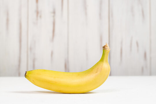 Yellow whole banana on a white wooden background.
