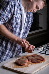 A man peppers a peppered steak. Cooking pepper steak on a wooden board. Juicy pepper steak. vertical photo