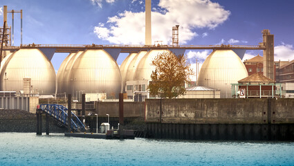 Large digestion towers for the treatment of wastewater at the edge of the port in bright sunny...