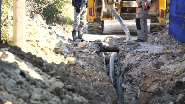 Plastic pipes laid in trenches. Workers are installing water pipeline under a city street in a trench. New pipeline in a process of building, under construction. Workers are laying pipeline. Close up
