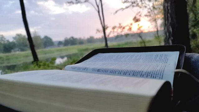 Man reading his bible, closeup view on river side. Moving camera gorizontally. Religious expirience talk with God every morning