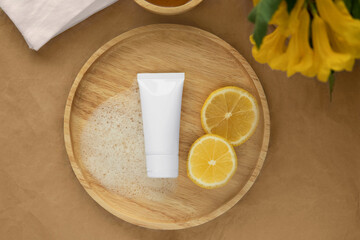 Obraz na płótnie Canvas Top down view or flat lay Organic gentle skincare product cleanser white tube with a blank label and soap smear on a wooden plate decoration with fresh leaves and yellow flower wrap paper background