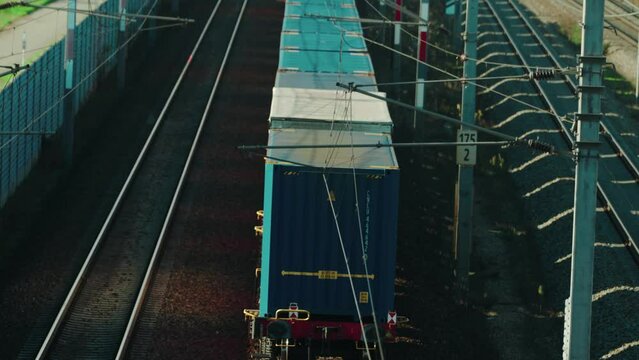 A slow freight train powered by electricity making its way through a rural area in Austria while being overtaken by a fast passenger train