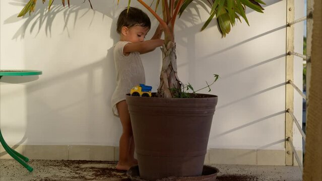 Cute latin baby boy using a blue toy broom to clean sweep the dirt from the floor after doing a mischief on a sunny afternoon
