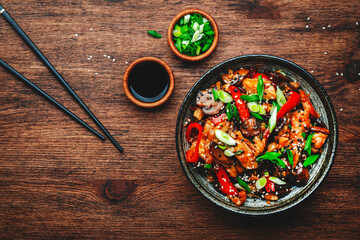 Stir fry chicken with paprika, mushrooms and chives in bowl. Asian cuisine dish. Wooden kitchen...