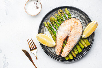 Baked steam salmon with asparagus and lemon on plate. White table background, top view