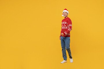 Fototapeta na wymiar Full body side view smiling fun merry young man wear red knitted Christmas sweater Santa hat posing walking going isolated on plain yellow background. Happy New Year 2023 celebration holiday concept.