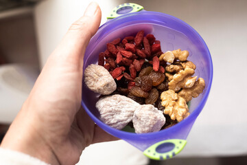 blu plastic cup with dried fruits and nuts. Walnuts, goji, figs and dark raisin mix for breakfast. Raw and healthy food contest. Natural vitamin products. Close up picture. Human hand holds a plate. 