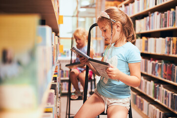 Schoolgirls looking for audio books in school library. Students choosing books. Elementary...