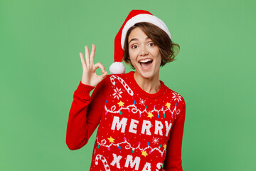 Merry smiling fun young woman 20s wear knitted xmas sweater Santa hat posing showing okay ok...