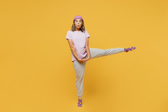 Full Body Young Woman With Duck Face Wears Purple Pyjamas Jam Sleep Eye Mask Rest Relax At Home Look Camera Raise Up Leg Posing Isolated On Plain Yellow Background Studio Portrait. Night Nap Concept.