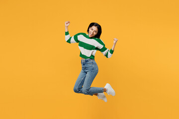 Fototapeta na wymiar Full body side view cool young latin woman wear casual cozy green knitted sweater jump high do winner gesture clench fist isolated on plain yellow background studio portrait People lifestyle concept.