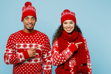 Merry young couple two fun man woman wear red Christmas sweater Santa hat posing point index finger aside on mock up isolated on plain pastel light blue background Happy New Year 2023 holiday concept