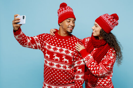 Merry young couple two man woman wear red Christmas sweater Santa hat posing doing selfie shot on mobile cell phone isolated on plain pastel light blue background. Happy New Year 2023 holiday concept.