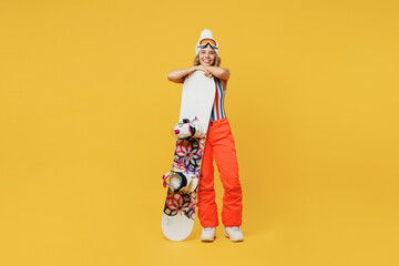 Snowboarder happy woman wear orange suit goggles mask hat ski costume swimsuit spend extreme hold snowboard weekend isolated on plain yellow background studio. Winter sport hobby trip relax concept.