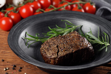 Medium rare roast beef with red tomatoes in a black plate on a rustic wooden table
