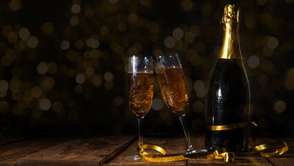 New Year Sylvester festive celebration holiday New Year's Eve greeting card - Champagne or sparkling wine bottle and glasses with golden ribbon on wooden table and bokeh lights in the background