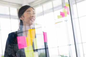 Group of successful Asian businesswomen teamwork. Brainstorm meeting with colorful sticky paper notes on the glass wall for new ideas. Using agile methodology for business in a tech start-up office.