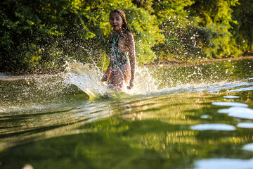 Teenage girl splashing green water of river lake in summer. Summer vacation fun.