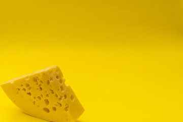 A piece of cheese with holes lies on a yellow background, monochrome products