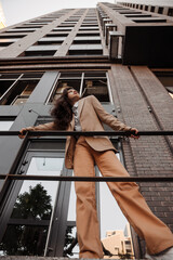 Obraz na płótnie Canvas Tall stylish girl with oversized jacket posing near the railing and steps on the city background