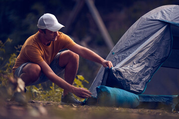 Man camping in nature, setting up the tent for overnight staying near forest river.