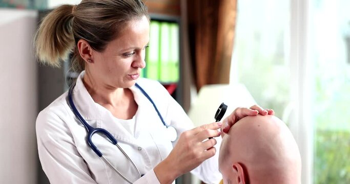 Trichologist examines bald man with alopecia with magnifying glass