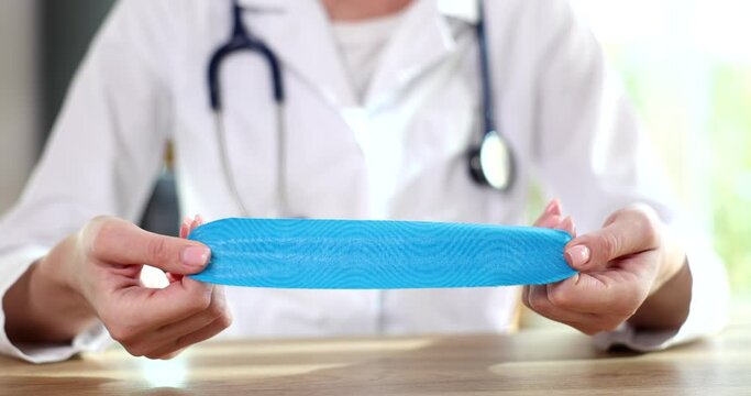 Female therapist doctor shows and advertises blue kinesiology physio tape for hand application