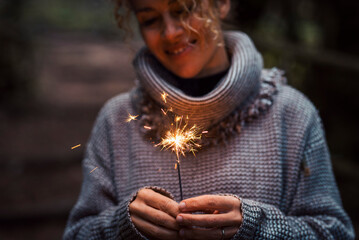 Front view of happy woman celebrating with sparkler light in outdoor. Foreground focus on fire and...