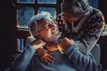Portrait of couple of senior people in love at home in the evening dark light. Old man smile at her mature woman wife hugging and enjoying relationship. Winter home background. Elderly people life