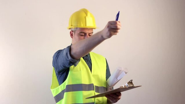 Construction architect wearing a yellow vest and hard hat is taking notes on the job site.