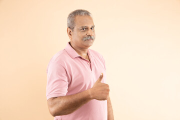 Portrait of happy indian senior man doing thumbs up over beige studio background, all good, okay...