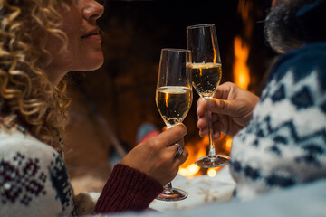 Side close up view of romantic couple celebrating together drinking champagne wine flutes in love and relationship. People man and woman celebrate new year eve in front of a fireplace holiday vacation