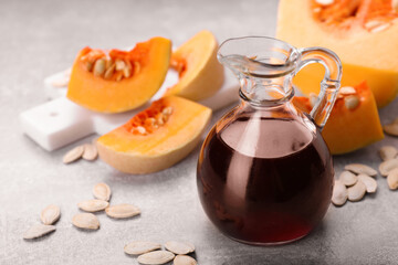 Fresh pumpkin seed oil in glass jug on grey table