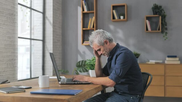 concerned stressed mature man works at the computer in office,side view of worried male at the desk having trouble at the laptop