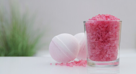 Glass with sea salt and bath bombs on table in bathroom, closeup. Space for text