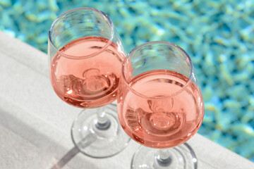 Glasses of tasty rose wine on swimming pool edge, closeup