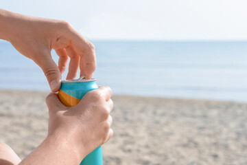Woman opening aluminum can with beverage on beach, closeup. Space for text